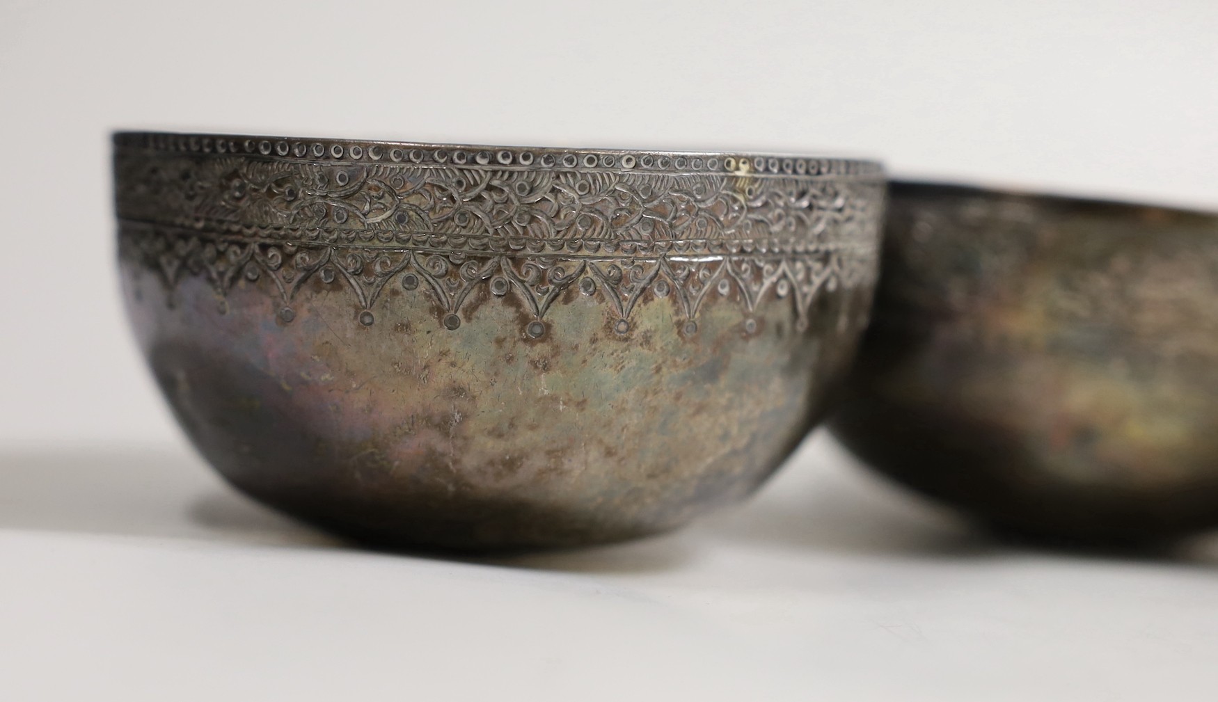 A Malay Straits pedestal bowl and cover or 'Batil Ber Tutop' (a.f.), three Malay Straits white metal betel nut cups and two similar small bowls, all with embossed floral or foliate designs (one cup with green enamelled d